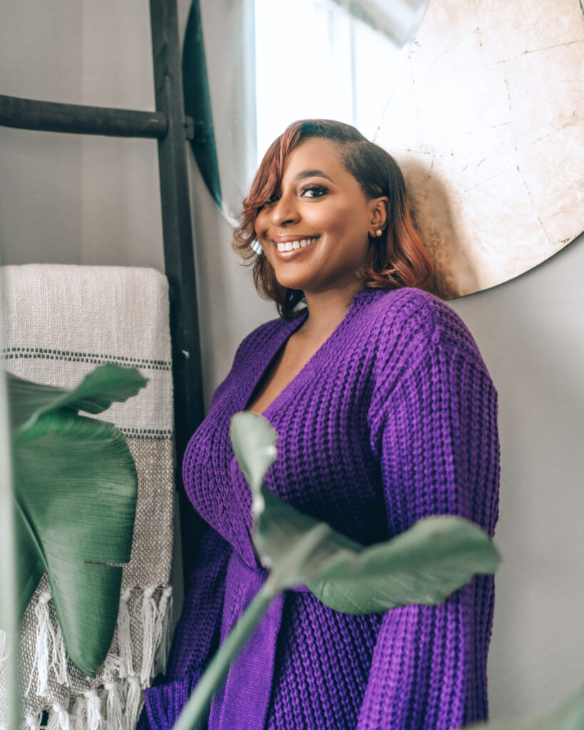 Woman wearing a purple sweater dress smiling and posing in front of mirror